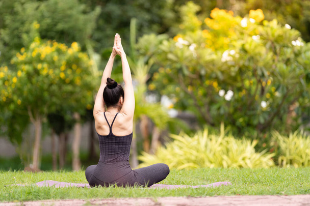Sebevědomá Asiatka středního věku ve sportovním oblečení, která ráno cvičí jógu na podložce na jógu venku na dvorku. Mladá žena dělá jóga cvičení venku v přírodním parku - Fotografie, Obrázek