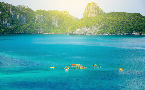 Aerial view a group of tourists kayaking on the blue sea with green island in the background. Kayaking at the tropical islands on sunny summer. Mu Koh Ang Thong National Park, Surat Thani, Thailand. Focus on kayak. - Foto, Imagen
