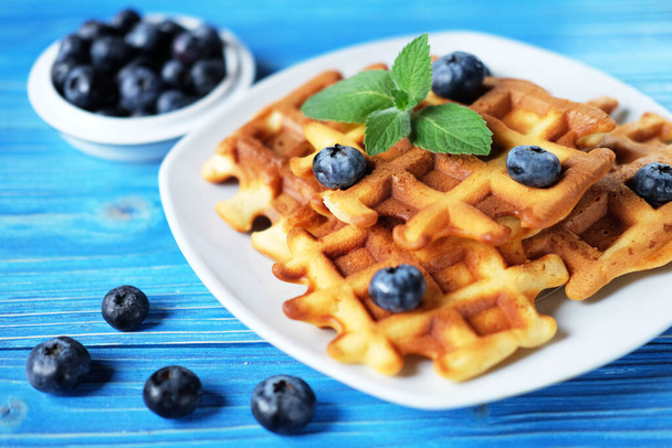 Traditional belgian waffles with fresh berrys and sugar powder on white plate, blue wooden background. Flat lay, top view, copy space. - Fotografie, Obrázek
