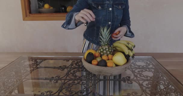 A woman finishes filling a fruit bowl with organic fresh fruits, oranges, banana, apples, mango, pineapple. Concept for healthy food and healthy living. - Metraje, vídeo