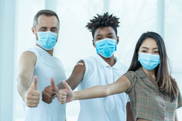 Multinationale Menschen, Teenager, afrikanische Männer, asiatische Frauen und weiße Männer mit Masken, die ihre Ärmel aufklappen und Plakate zeigen, auf denen Nadelstiche für den COVID-19-Impfstoff zu sehen sind.  - Foto, Bild