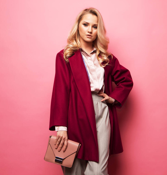 Beautiful woman long blond curly hair wear casual coat and holding handbag over pink background - Photo, image