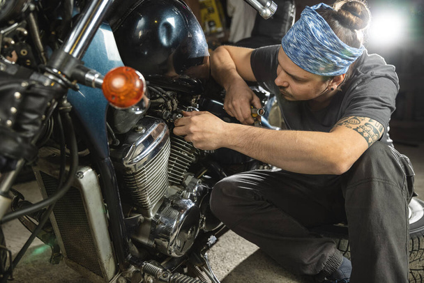 バンダナの若い整備士がヴィンテージバイクを修理する。肖像画、クローズアップ. - 写真・画像