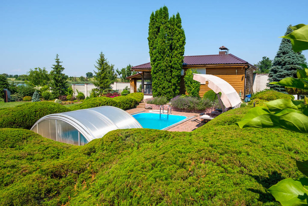 Garden with nicely trimmed bushes and stones and swimming pool in backyard. Landscape design. High quality photo - Photo, Image