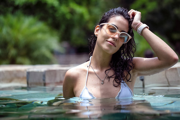 Модель брюнетки с мокрыми волосами, темными очками и белым бикини. Бразильская девушка Отдых. здоровой жизни. Жаркий день. Окунуться в бассейн в солнечный день - Фото, изображение
