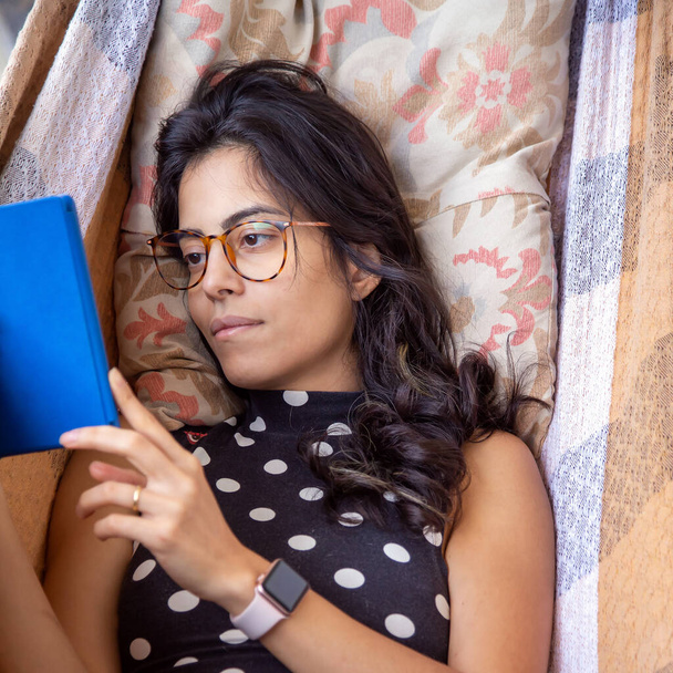 Een brunette met een bril op die een boek leest over een e-reader. Laserstraal. Cultuur. - Foto, afbeelding