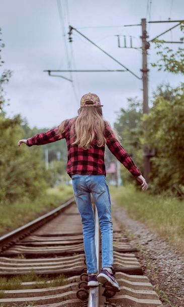 Holčička na kolejích. Dívka na železnici v džínách, čepici a košili v cele. Zadní pohled.  - Fotografie, Obrázek