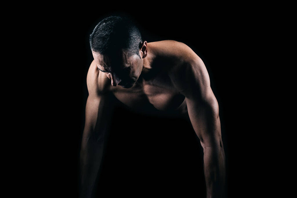 Muscular man doing push-ups with black background - Foto, afbeelding