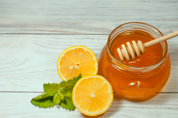frischer Honig in einem transparenten Glas auf Holzgrund und Zitrone mit Minze, gesunder Lebensstil - Foto, Bild
