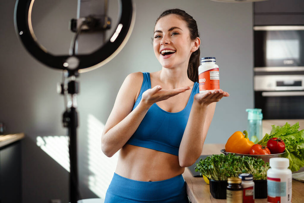 Helathy smiling brunette woman blogger advertising healthy organic supplements while standing in front of a camera - Photo, image