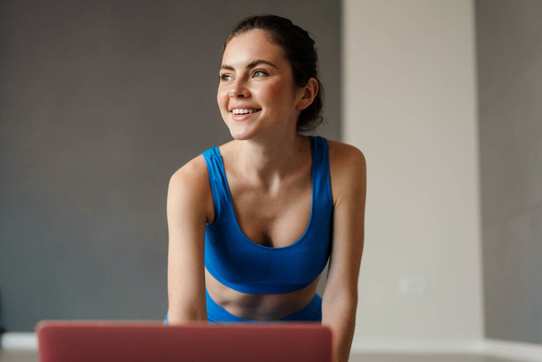 White smiling woman using laptop during yoga practice at home - Fotoğraf, Görsel