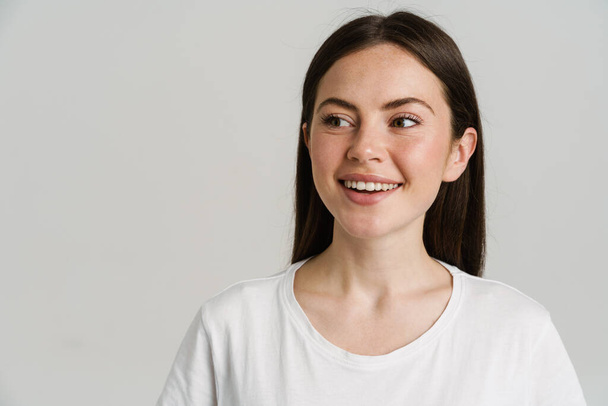 Young brunette woman in t-shirt smiling and looking aside isolated over white background - Fotoğraf, Görsel