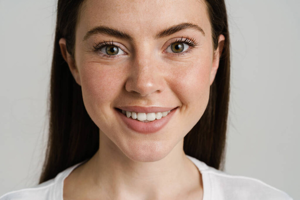 Young brunette woman in t-shirt smiling and looking at camera isolated over white background - Foto, Imagem