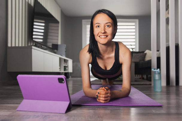 Young woman doing plank exercise and looking at the camera with a smile - Foto, Imagem
