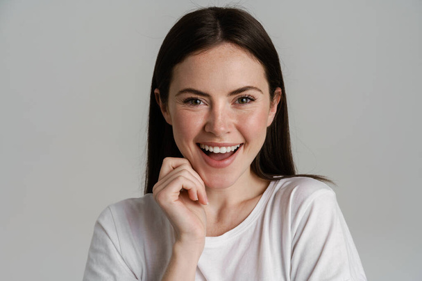 Young brunette woman in t-shirt smiling and looking at camera isolated over white background - Foto, afbeelding