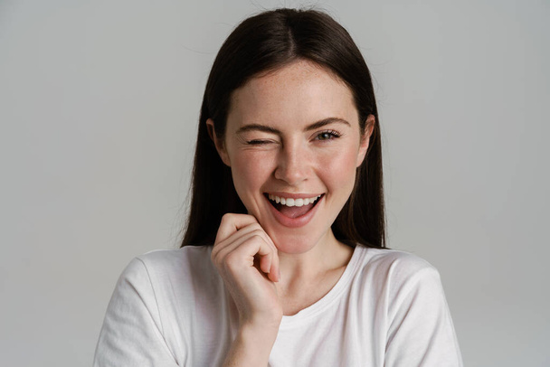 Young brunette woman winking and laughing at camera isolated over white background - Photo, Image
