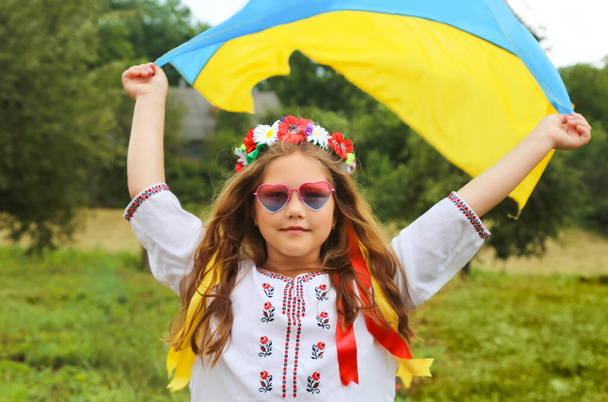 Keltainen ja sininen lippu Ukrainan käsissä kaunis tyttö kirjailtu paita ja seppele nauhoilla. Lapsi vehnäpellolla. Ukrainan itsenäisyyspäivä, lippu, perustuslaki, kirjonta. Banneri - Valokuva, kuva