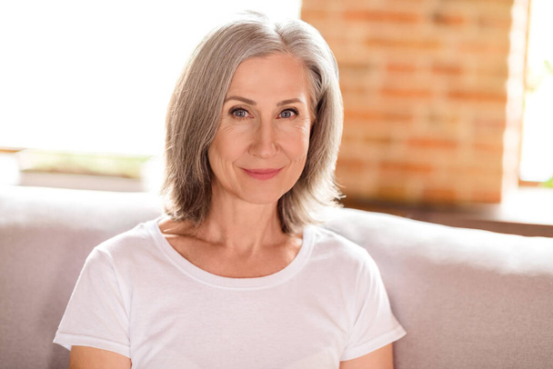 Portrait of attractive cheery healthy grey-haired woman sitting on sofa calm life day daydream at home house indoors modern loft brick interior - Photo, image