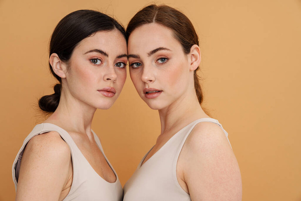 Young two women in undershirt posing and looking at camera isolated over yellow background - Foto, Bild