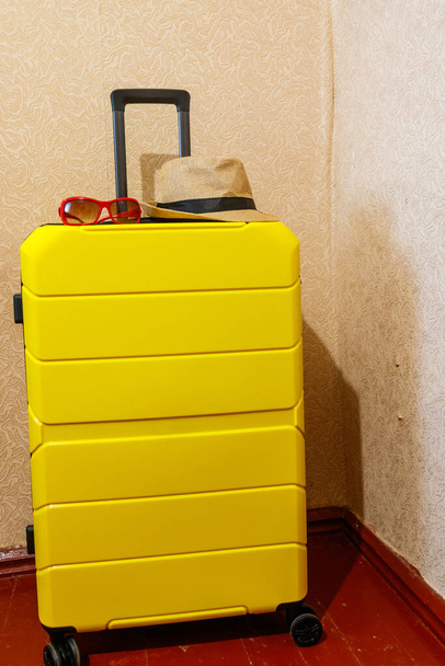 Maleta amarilla con gafas de sol y sombrero en una habitación. Concepto de viaje - Foto, Imagen