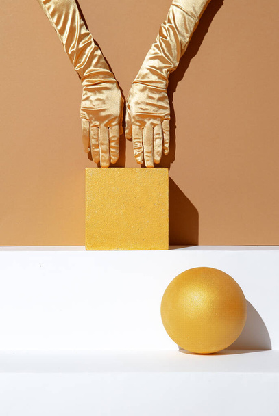 Minimalistic geometry scene. Hand in golden gloves and cube and ball decoration. Trendy beige and gold colours. Seasonal fall winter wallpaper. - Valokuva, kuva