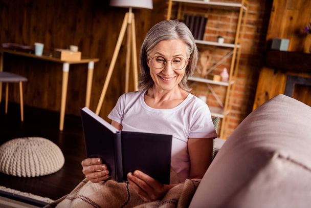 Portrait of attractive cheerful focused grey-haired woman sitting on divan reading interesting book at home house flat indoors - Fotografie, Obrázek