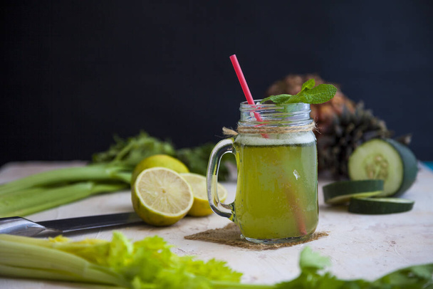 A glass of green citrus lemonade with a red stick surrounded by lime, lemon, cucumber, and greens - Zdjęcie, obraz