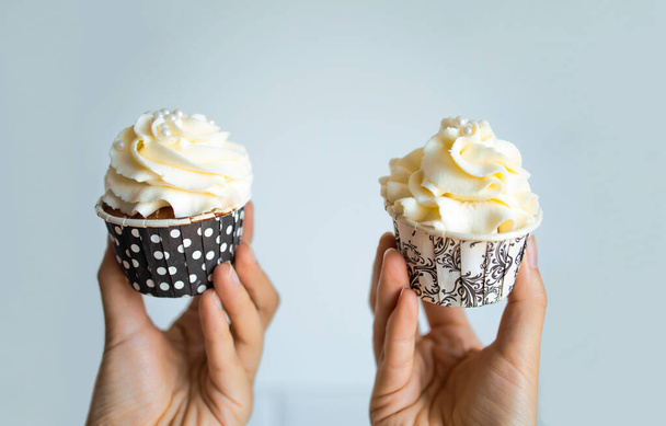 A Female Hand Holds A Cupcake With Cream On Blue Background. - 写真・画像