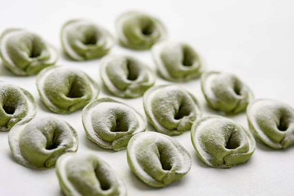 A closeup of beautiful freshly made green cappelletti covered in flour on a bright white background - 写真・画像