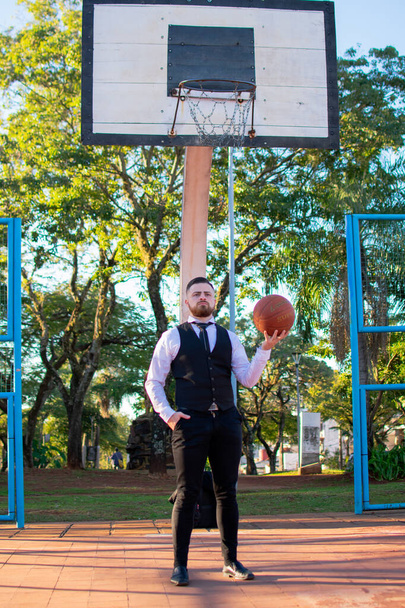 A young Hispanic male in an elegant suit standing on a sports ground with a basketball ball - Photo, image