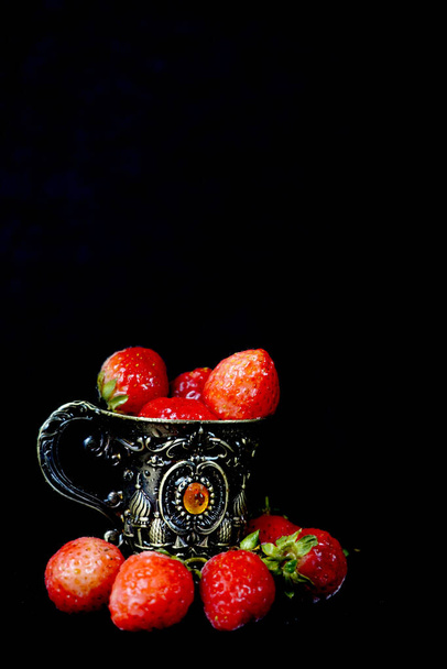 Um tiro vertical de morangos maduros deliciosos em uma xícara de metal vintage isolado em um fundo preto - Foto, Imagem