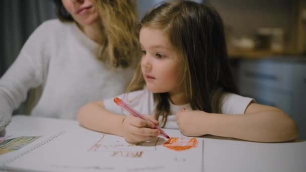 Une mère et une petite fille dessinent des dessins sur papier dans la cuisine avec des marqueurs - Séquence, vidéo