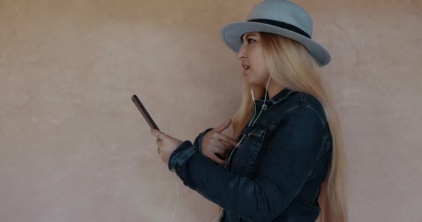 Side-profile, young attractive woman with hat listening to music from cellphone, singing along, wearing headphones. Real-time footage. - Metraje, vídeo