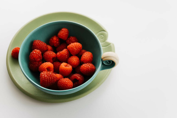 A bowl of juicy raspberries on a white surface - Fotoğraf, Görsel
