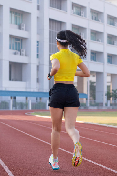 Młoda Azjatka biegnie biegając po bieżni na stadionie miejskim w słoneczny poranek, aby utrzymać kondycję i zdrowy tryb życia. Młoda trenerka biegnie po stadionie. Sport i rekreacja - Zdjęcie, obraz
