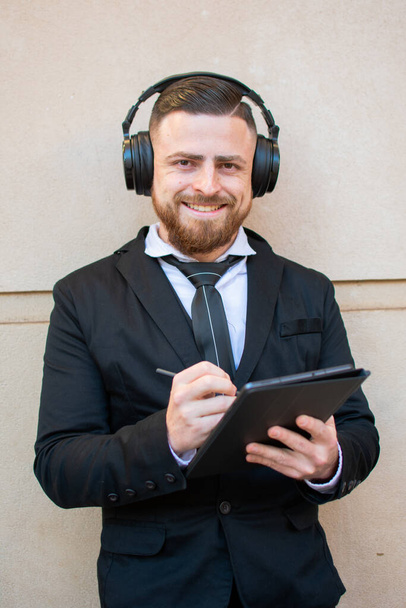 A young male in an elegant suit and big headphones using a tablet - Zdjęcie, obraz