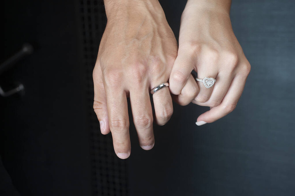A closeup image of male and female hands with silver rings holding their fingers on a black background - Zdjęcie, obraz