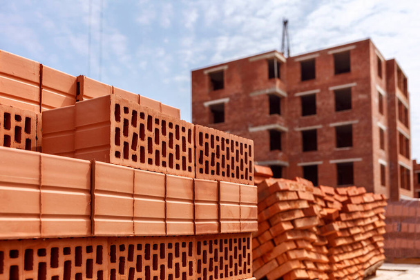 Stack of red clay brick on construction site on multistory building background. - Photo, Image