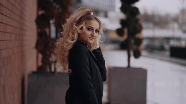 The beautiful blonde, beautiful make-up, office style, subtly arranges her hair, under the severe wind, is isolated outside under the blurred urban landscape. Female energy. Beauty industry. Artistic - Footage, Video