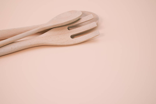 A wooden spoons and fork isolated on a peach background with free space for text - Fotó, kép