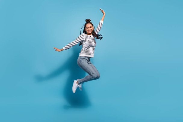 полноразмерный профиль боковая фотография молодой жизнерадостной африканской девушки счастливой положительной улыбкой весело прыгать на голубом цветном фоне - Фото, изображение