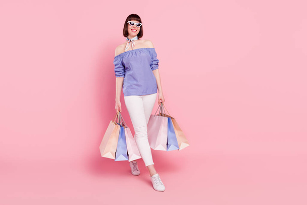 Full length body size photo woman keeping bargains after shopping in mall smiling isolated on pastel pink color background - Fotó, kép