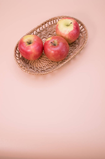 A vertical shot of fresh apples on a woven tray isolated on pink background with copyspace - Foto, Imagen