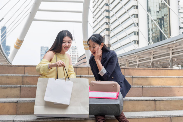 Two young asian woman excited holding shopping bags and looking on stair in urban - 写真・画像