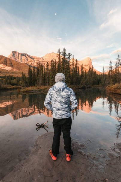 カナダのキャンモアで秋に川に映る三姉妹山の景色を楽しむ男旅行者 - 写真・画像
