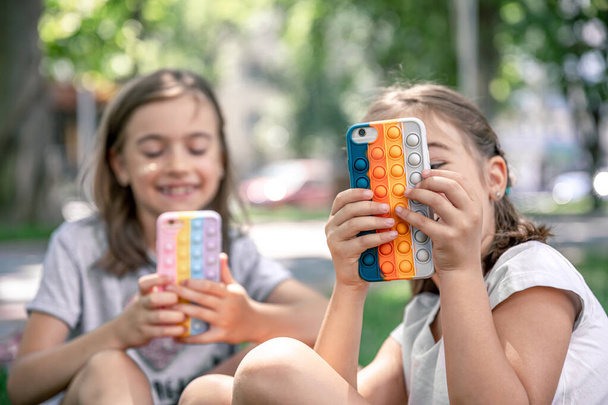 Kleine meisjes buiten met telefoons in een geval met puistjes pop it, een trendy anti stress speelgoed. - Foto, afbeelding