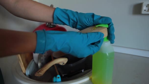 Una mujer con delantal y guantes de goma lava los platos sucios en el fregadero de su cocina. Platos sucios en un fregadero para lavar. - Metraje, vídeo