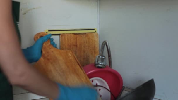 Μια γυναίκα με ποδιά και λαστιχένια γάντια πλένει βρώμικα πιάτα στο νεροχύτη της κουζίνας της. Βρώμικα πιάτα στο νεροχύτη για πλύσιμο. - Πλάνα, βίντεο