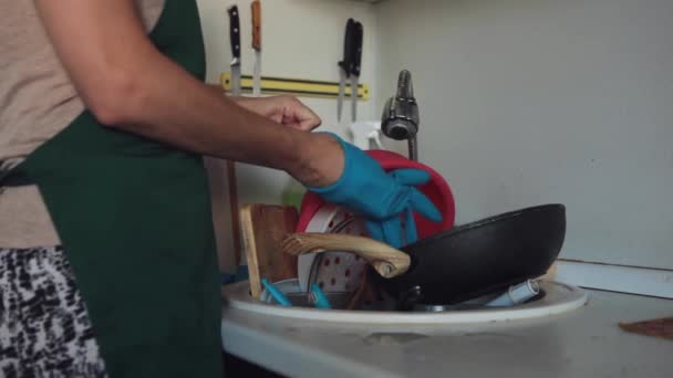 Uma mulher de avental e luvas de borracha lava pratos sujos na pia da cozinha. Pratos sujos em uma pia para lavar a louça. - Filmagem, Vídeo