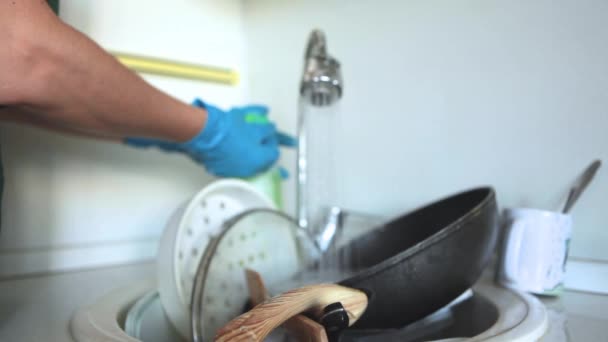 Una donna in grembiule e guanti di gomma lava i piatti sporchi nel lavandino della sua cucina. Piatti sporchi in un lavandino per lavare. - Filmati, video